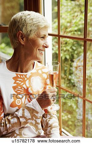 Stock Photo - Senior woman holding a champagne flute and smiling. Fotosearch