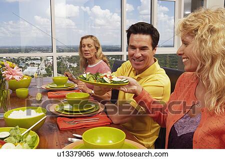 Stock Photography - Close-up of a mature couple and a mid adult woman sitting at the dining table. Fotosearch