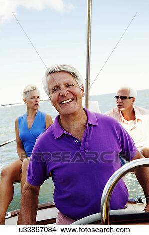 Close-up of a mature man driving a boat with a mature couple sitting behind him View Large Photo Image Picture - Close-up of a mature man driving a boat with a mature couple sitting behind him. Fotosearch