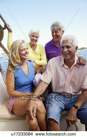 Picture - Close-up of two mature couples sitting in a boat and smiling. Fotosearch