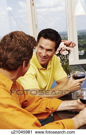 Stock Image - Close-up of two mature men holding glasses of wine and talking. Fotosearch