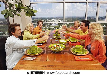 Group of people sitting at the dining table and toasting a drink View Large Photo Image Picture - Group of people sitting at the dining table and toasting a drink. Fotosearch