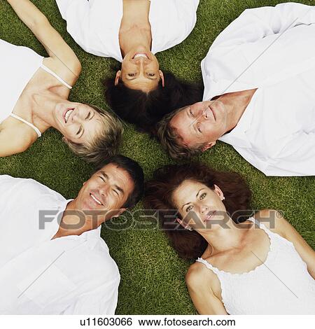 Stock Photograph - High angle view of two mature men and three mature women lying on the grass. Fotosearch