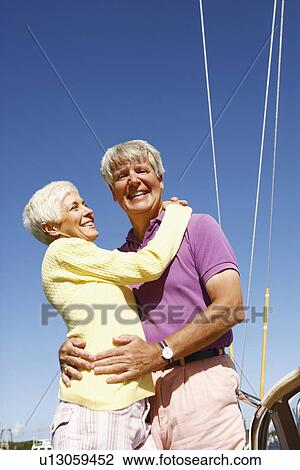 Stock Image - Low angle view of a mature couple embracing each other and smiling. Fotosearch