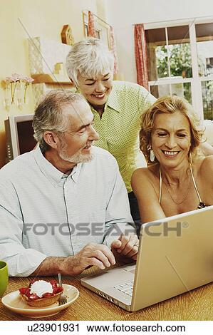 Stock Image - Mature couple and a senior woman smiling in front of a laptop. Fotosearch