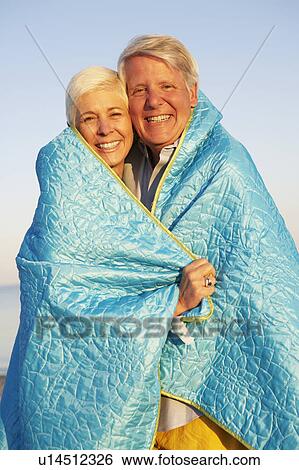 Stock Photograph - Portrait of a mature couple wrapped in a blanket and smiling. Fotosearch
