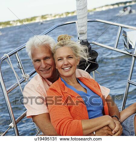 Stock Image - Portrait of a mature man embracing a mature woman from behind in a boat and smiling. Fotosearch
