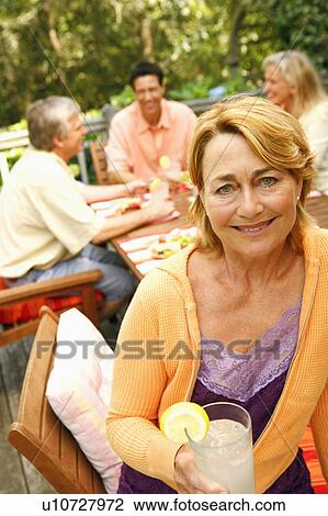 Stock Image - Portrait of a mature woman holding a glass of lemonade and smiling. Fotosearch