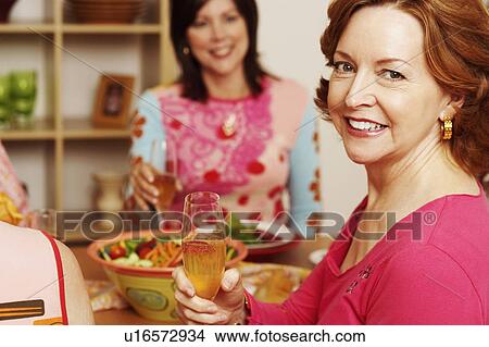 Portrait of a mature woman sitting at the dining table with her friend holding a champagne flute View Large Photo Image Picture - Portrait of a mature woman sitting at the dining table with her friend holding a champagne flute. Fotosearch