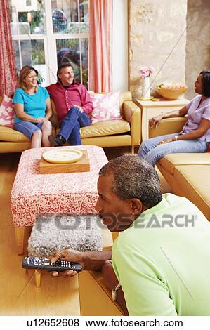 Stock Photo - Rear view of a mature man operating a remote control with three people sitting beside him. Fotosearch
