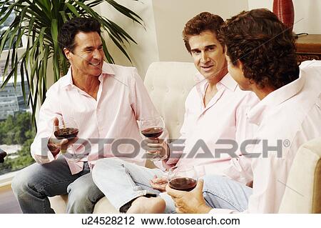Stock Image - Three mature men sitting together and holding glasses of wine. Fotosearch