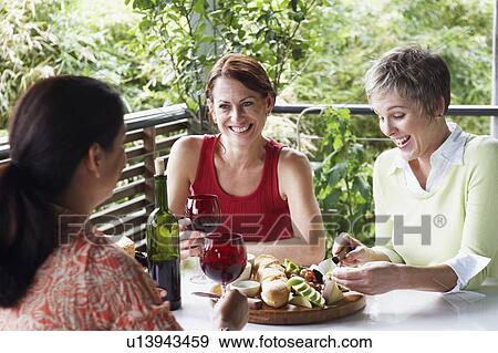 Stock Photo - Three mature women sitting at the table and smiling. Fotosearch