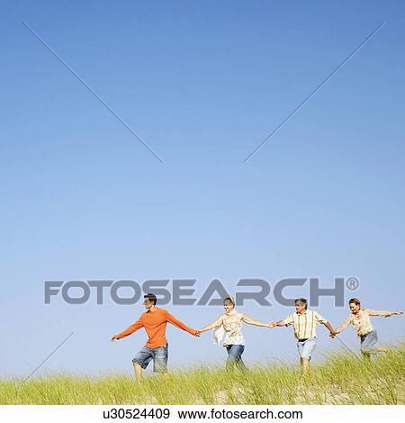 Stock Photo - Two mature couples holding hands and walking on a landscape. Fotosearch