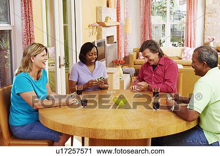 Stock Image - Two mature couples sitting at the table and playing cards. Fotosearch