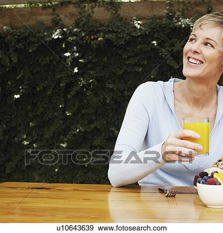 Stock Photo - Close-up of a mature woman holding a glass of orange juice. Fotosearch