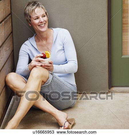 Stock Image - Close-up of a mature woman sitting in corner and holding a bowl of fruit. Fotosearch