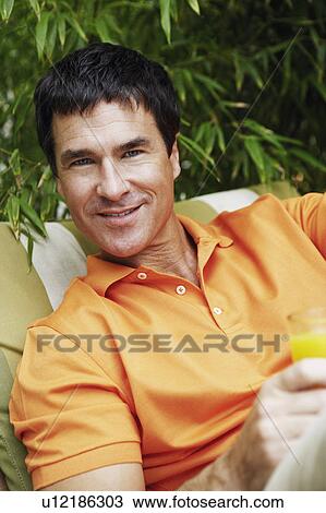 Stock Image - Portrait of a mature man holding a glass of juice. Fotosearch
