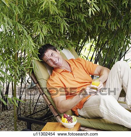 Portrait of a mature man reclining on a lounge chair and holding a glass of juice View Large Photo Image Picture - Portrait of a mature man reclining on a lounge chair and holding a glass of juice. Fotosearch