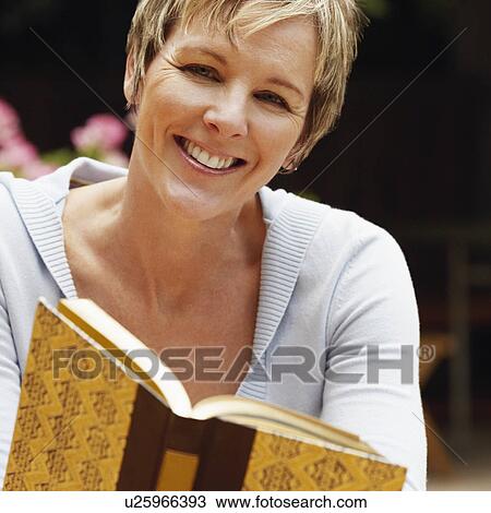 Stock Image - Portrait of a mature woman holding a book and smiling. Fotosearch