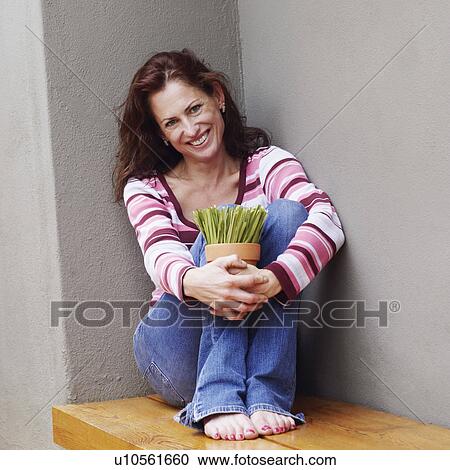 Stock Image - Portrait of a mature woman sitting on bench and holding a potted plant. Fotosearch