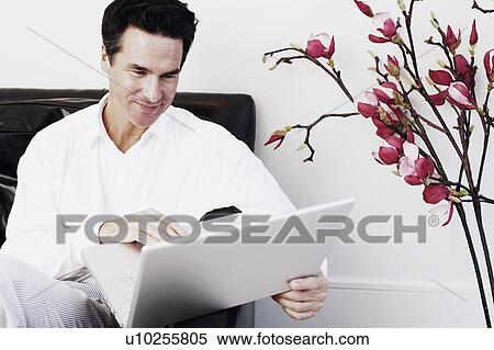 Stock Photography - Close-up of a mature man sitting on a couch and using a laptop. Fotosearch