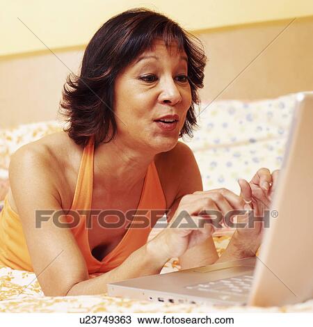 Close-up of a mature woman lying on the bed and using a laptop View Large Photo Image Stock Image - Close-up of a mature woman lying on the bed and using a laptop. Fotosearch