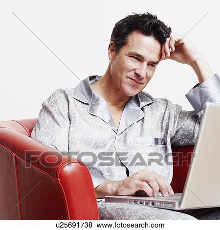 Stock Photo - Mature man sitting in an armchair and using a laptop. Fotosearch