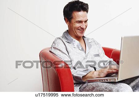 Stock Photography - Mature man sitting in an armchair and using a laptop. Fotosearch