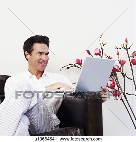 Mature man sitting on a couch and using a laptop View Large Photo Image Stock Image - Mature man sitting on a couch and using a laptop. Fotosearch