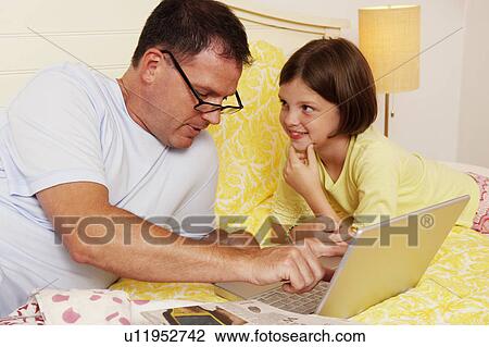 Stock Image - Mature man using a laptop with his daughter lying beside him. Fotosearch