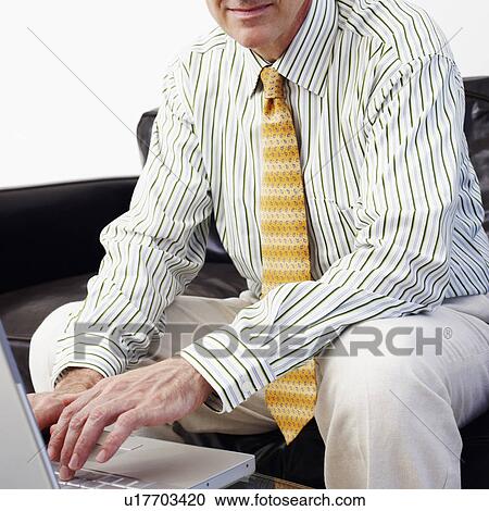 Portrait of a businessman sitting on a couch and using a laptop View Large Photo Image Stock Image - Portrait of a businessman sitting on a couch and using a laptop. Fotosearch