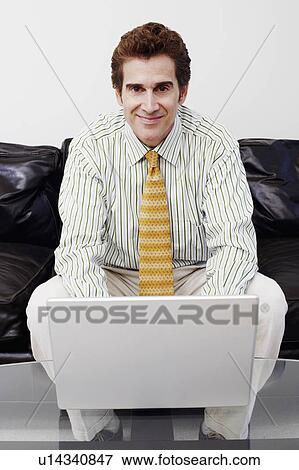 Portrait of a businessman sitting on a couch and using a laptop View Large Photo Image Stock Photo - Portrait of a businessman sitting on a couch and using a laptop. Fotosearch