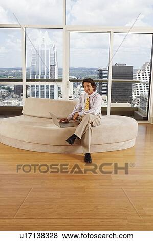Stock Photo - Portrait of a businessman sitting on a couch using a laptop. Fotosearch