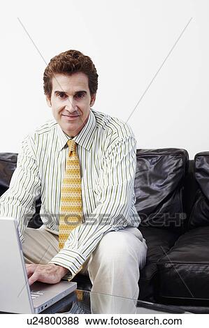 Stock Photo - Portrait of a businessman sitting on a couch and using a laptop. Fotosearch