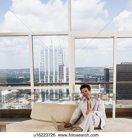 Stock Photograph - Portrait of a businessman sitting on a couch with a laptop. Fotosearch