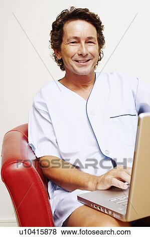 Portrait of a mature man sitting in an armchair and using a laptop View Large Photo Image Stock Photo - Portrait of a mature man sitting in an armchair and using a laptop. Fotosearch