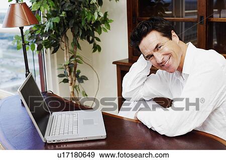 Stock Photo - Portrait of a mature man sitting in front of a laptop and smiling. Fotosearch