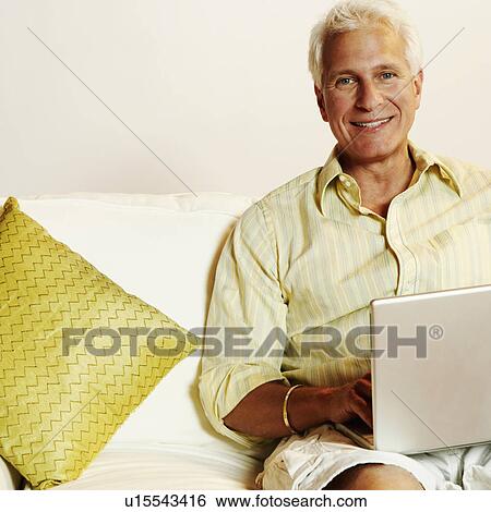 Portrait of a mature man sitting on a couch and using a laptop View Large Photo Image Stock Photograph - Portrait of a mature man sitting on a couch and using a laptop. Fotosearch