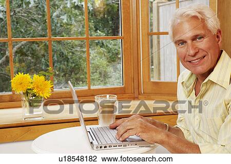 Stock Image - Portrait of a mature man using a laptop and smiling. Fotosearch
