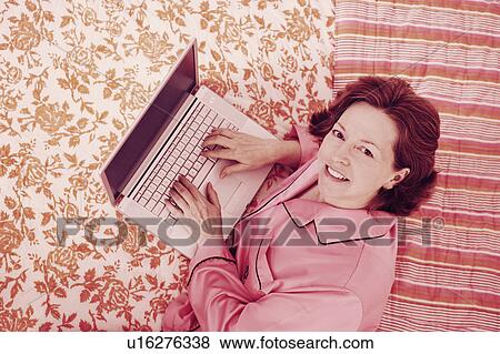 Portrait of a mature woman lying in bed and using a laptop View Large Photo Image Stock Photo - Portrait of a mature woman lying in bed and using a laptop. Fotosearch
