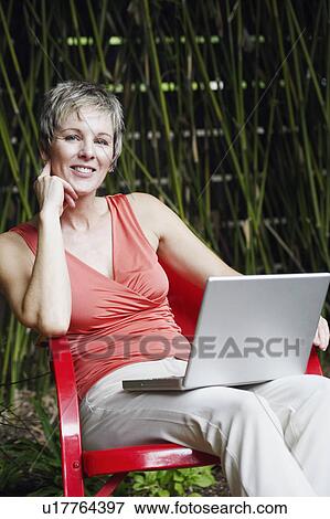 Portrait of a mature woman sitting on a chair with a laptop on her lap View Large Photo Image Stock Photo - Portrait of a mature woman sitting on a chair with a laptop on her lap. Fotosearch