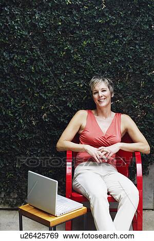 Portrait of a mature woman sitting on a chair and smiling View Large Photo Image Stock Photo - Portrait of a mature woman sitting on a chair and smiling. Fotosearch
