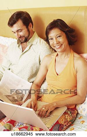 Portrait of a mature woman using a laptop with a mature man reading a newspaper beside her View Large Photo Image Stock Photography - Portrait of a mature woman using a laptop with a mature man reading a newspaper beside her. Fotosearch