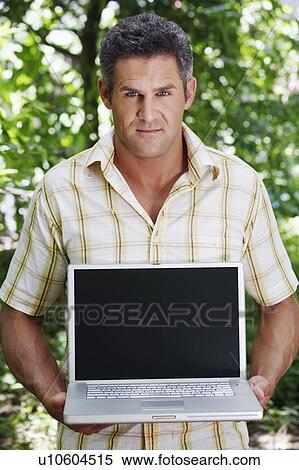 Stock Photography - Portrait of a mid adult man holding a laptop. Fotosearch