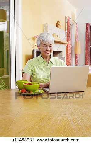 Stock Image - Senior woman using a laptop and smiling. Fotosearch