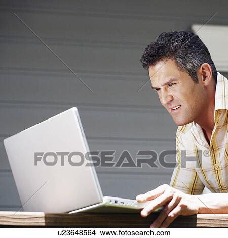 Picture - Side profile of a mid adult man using a laptop. Fotosearch