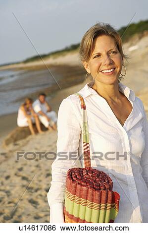 Close-up of a mature woman carrying a beach mat and smiling on the beach View Large Photo Image Stock Photograph - Close-up of a mature woman carrying a beach mat and smiling on the beach. Fotosearch