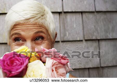 Stock Image - Close-up of a mature woman holding a bunch of flowers in front of her face and looking up. Fotosearch