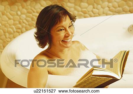 Stock Photo - Close-up of a mature woman sitting in a bathtub and holding a book. Fotosearch