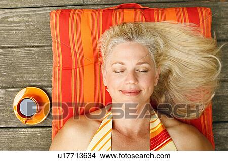 Picture - High angle view of a mature woman lying on her back with her eyes closed. Fotosearch
